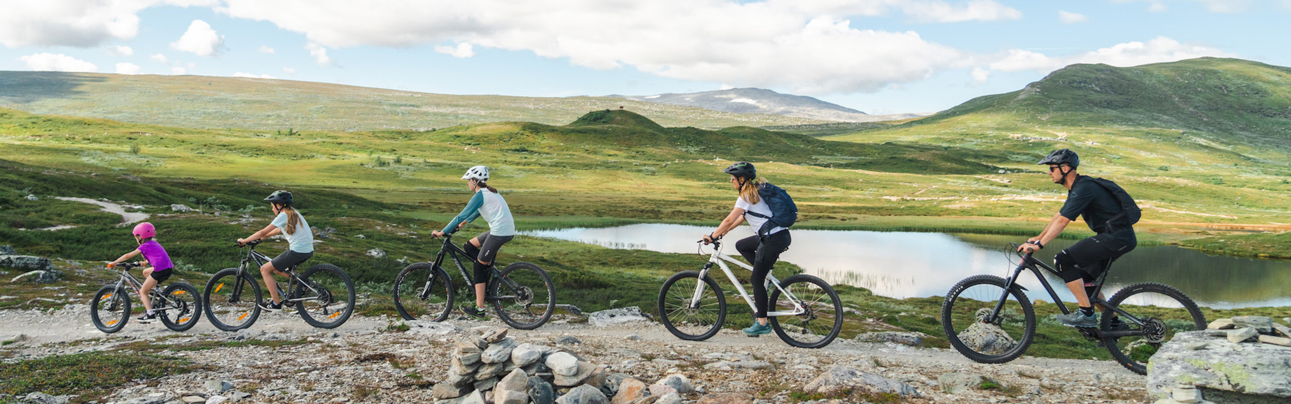 Familj med två vuxna och tre barn cyklar mountainbike på fjället i Tänndalen.