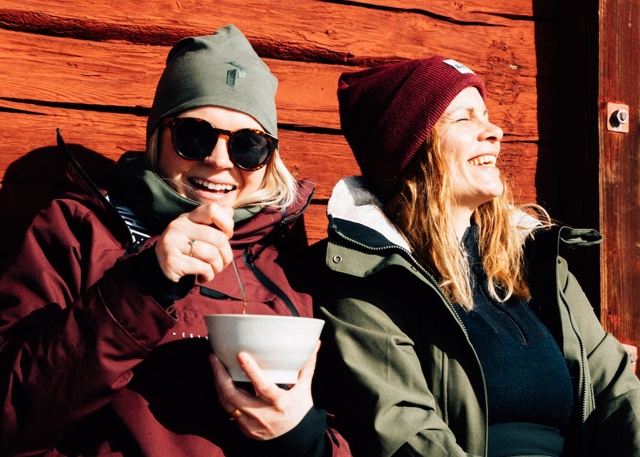 Två kvinnor njuter av solen mot en vägg i Tänndalen.