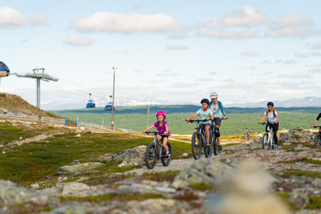Familj cyklar på fjället med sittlift i bakgrunden